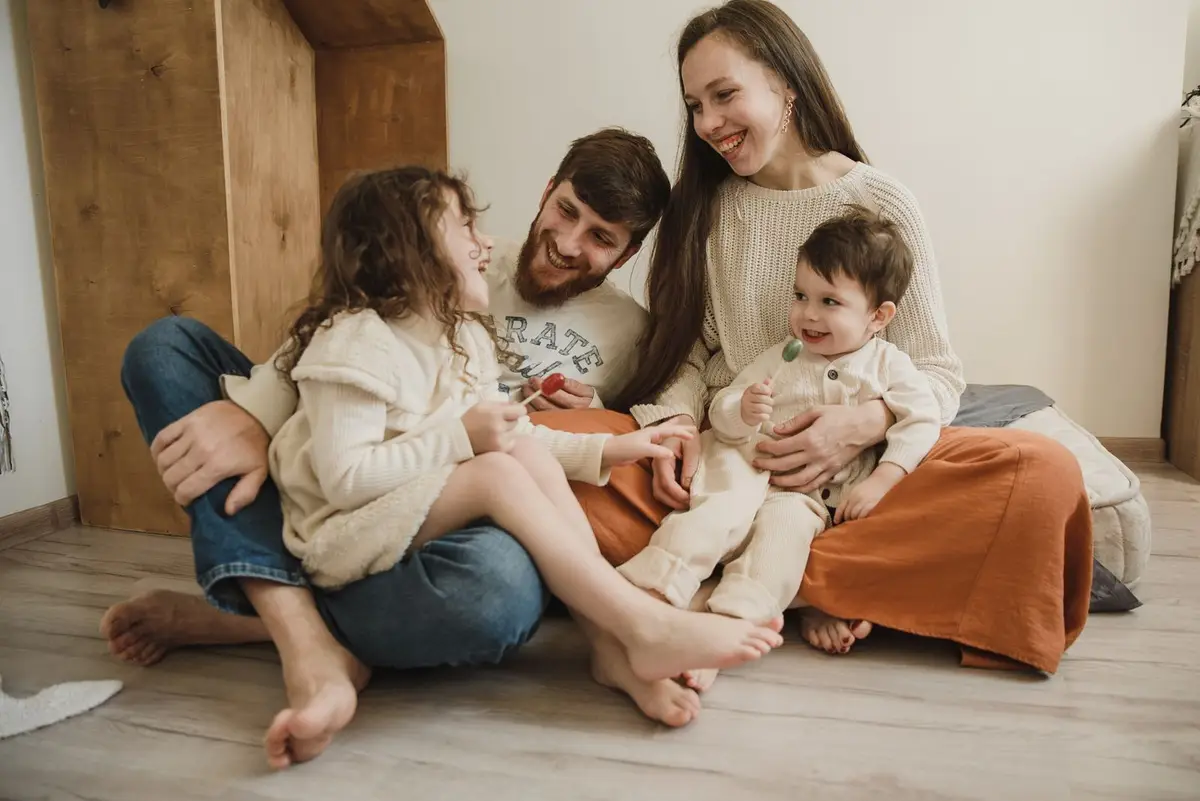 A family of four sitting together on the floor at home